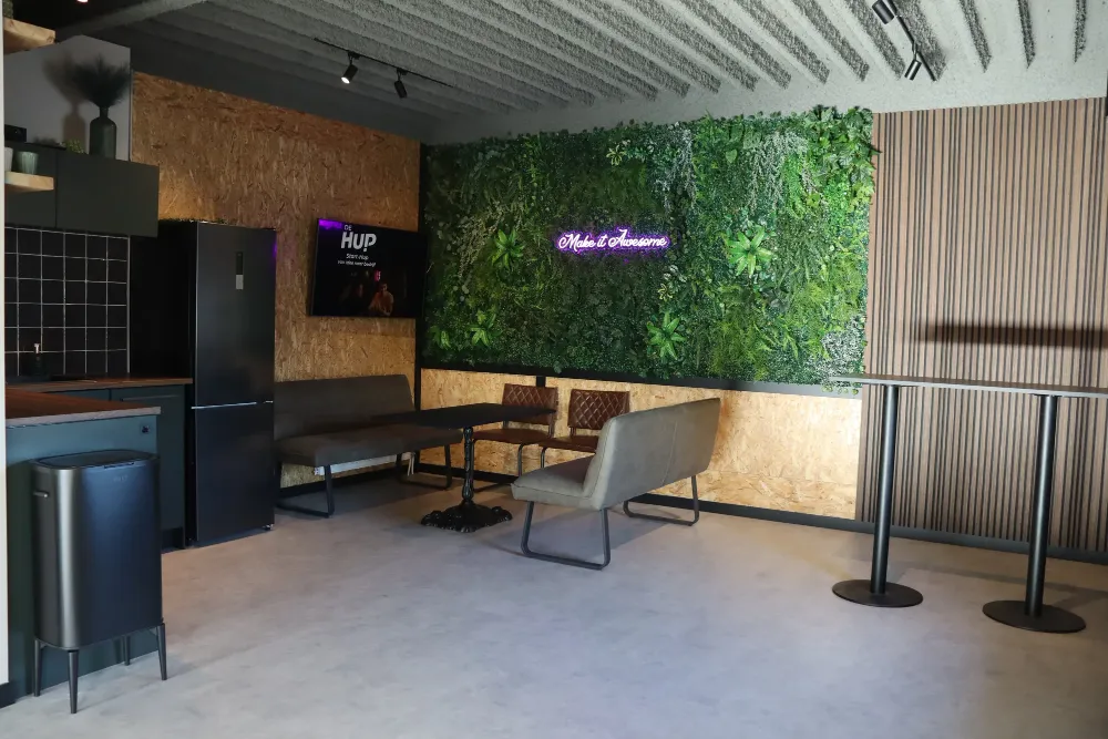 De lounge van De HUP met plantenwand, keuken en neonbord Make it Awesome