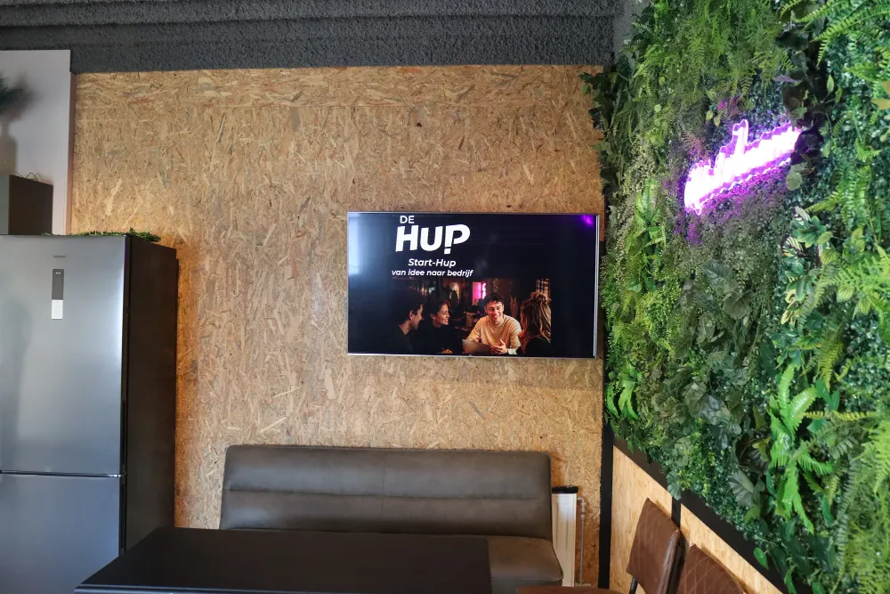 Scherm met De HUP logo naast de plantenwand