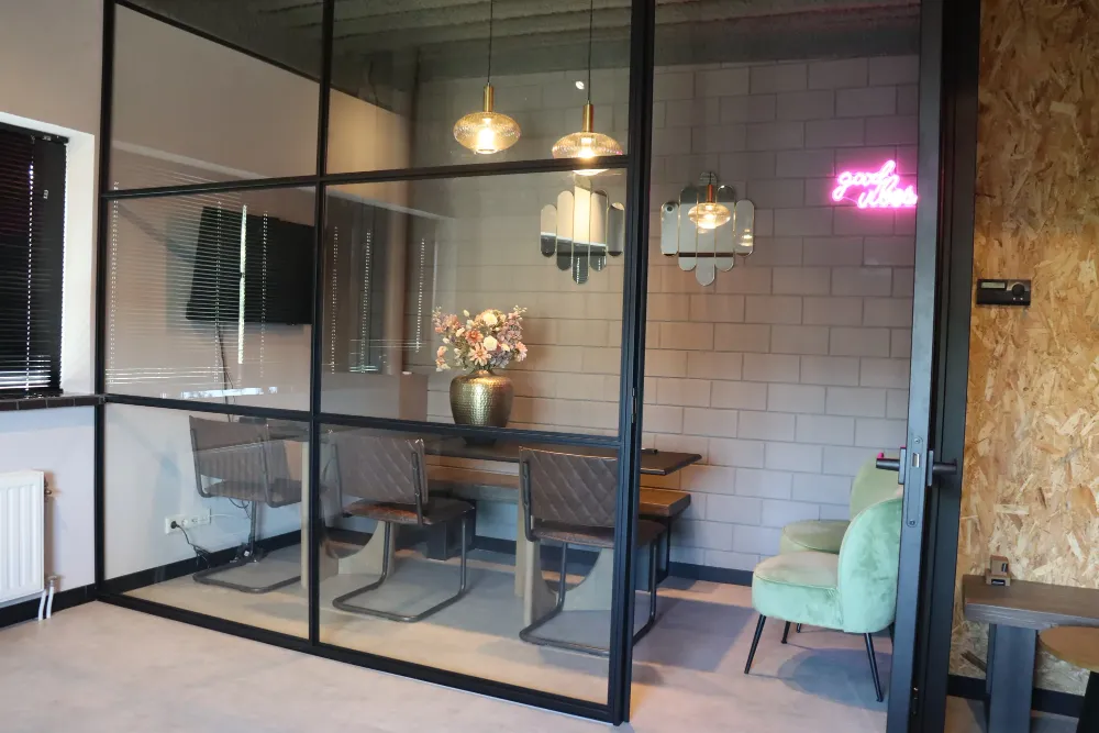 Overlegruimte achter stalen glaswand met good vibes neon